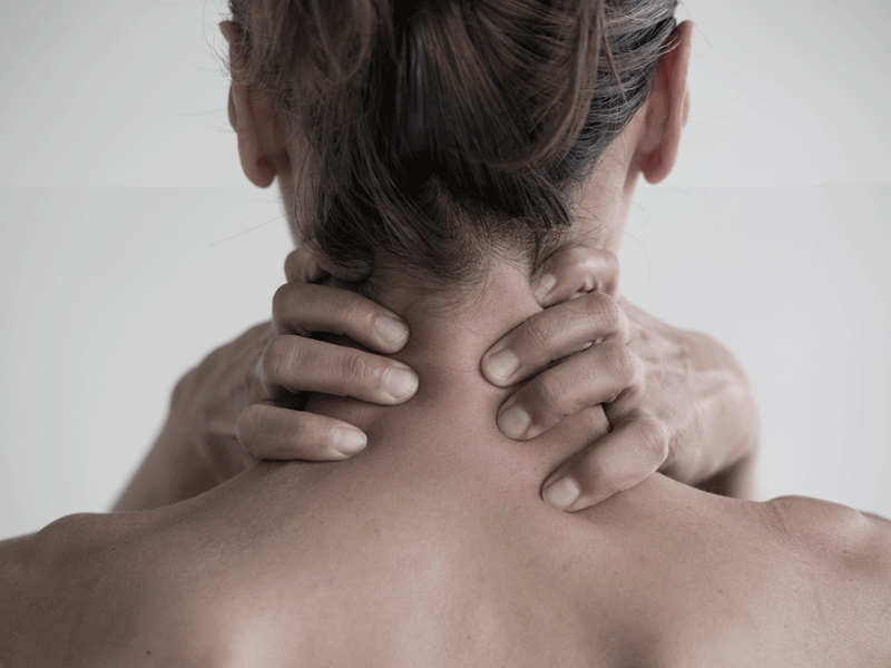 Mujer de espaldas con manos agarrando el cuello por dolor de cervicales