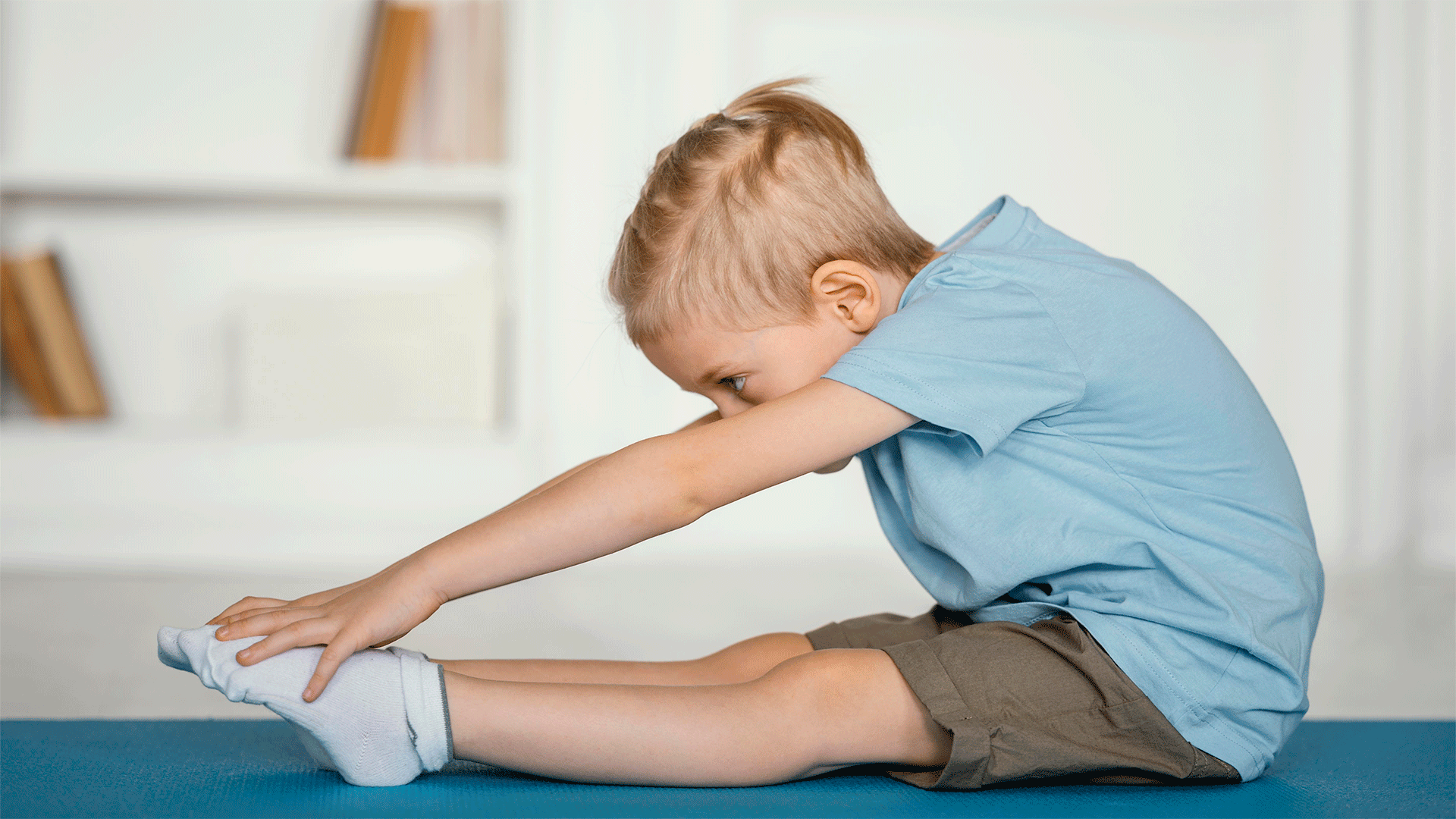 Niño rubio sentado estirando e intentado cogerse los dedos de los pies en Fernando Arco Centro de Fisioterapia en Almería