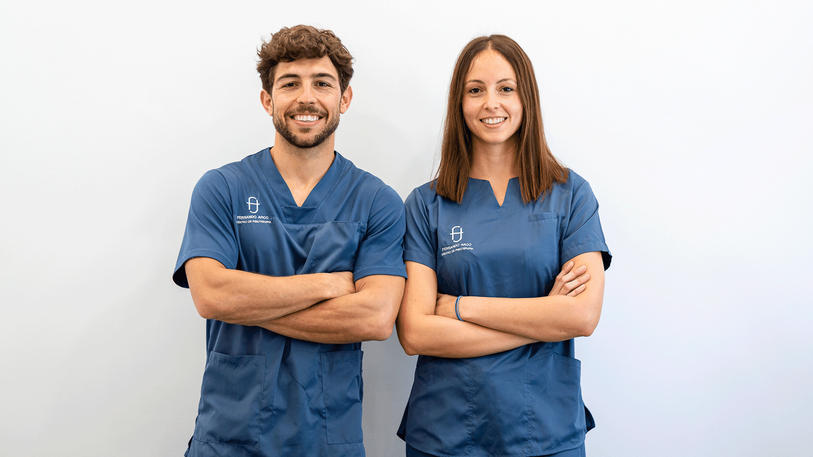 Equipo de Fisioterapeutas en Almería de Fernando Arco Centro de Fisioterapia en Almería posando para una foto con brazos cruzados y traje azul con fondo blanco